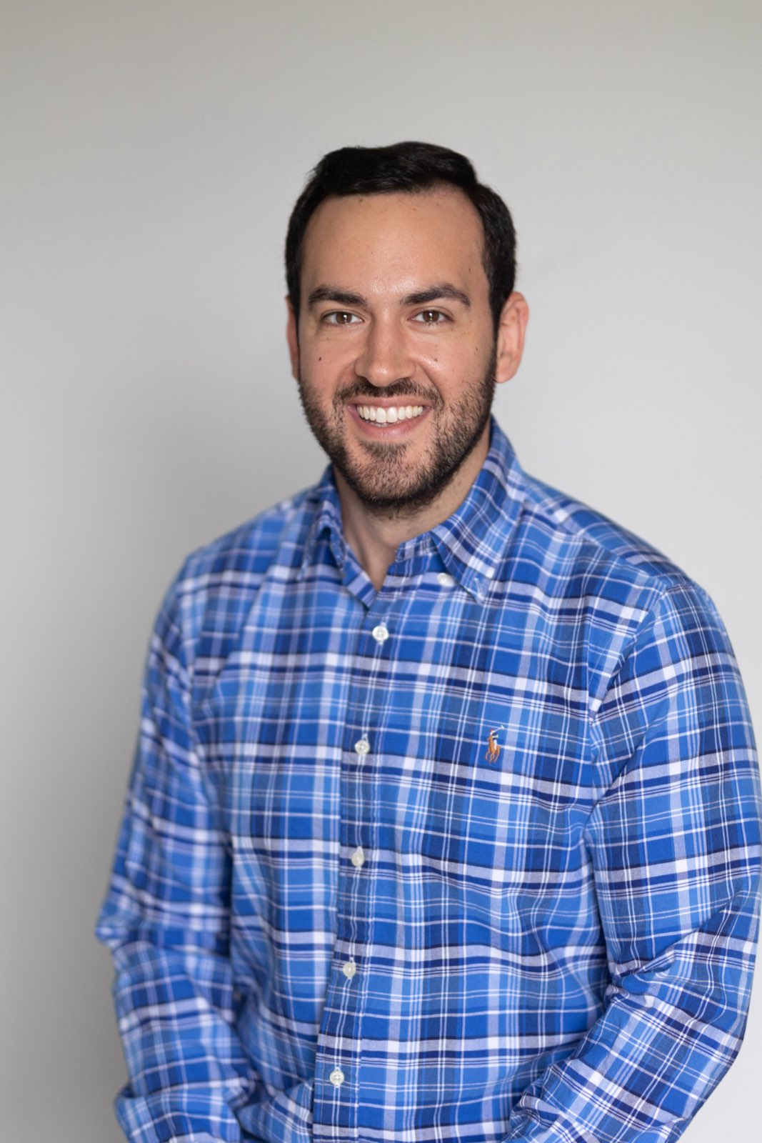 A man in a blue plaid shirt and a white shirt with a collar, smiling at the camera.