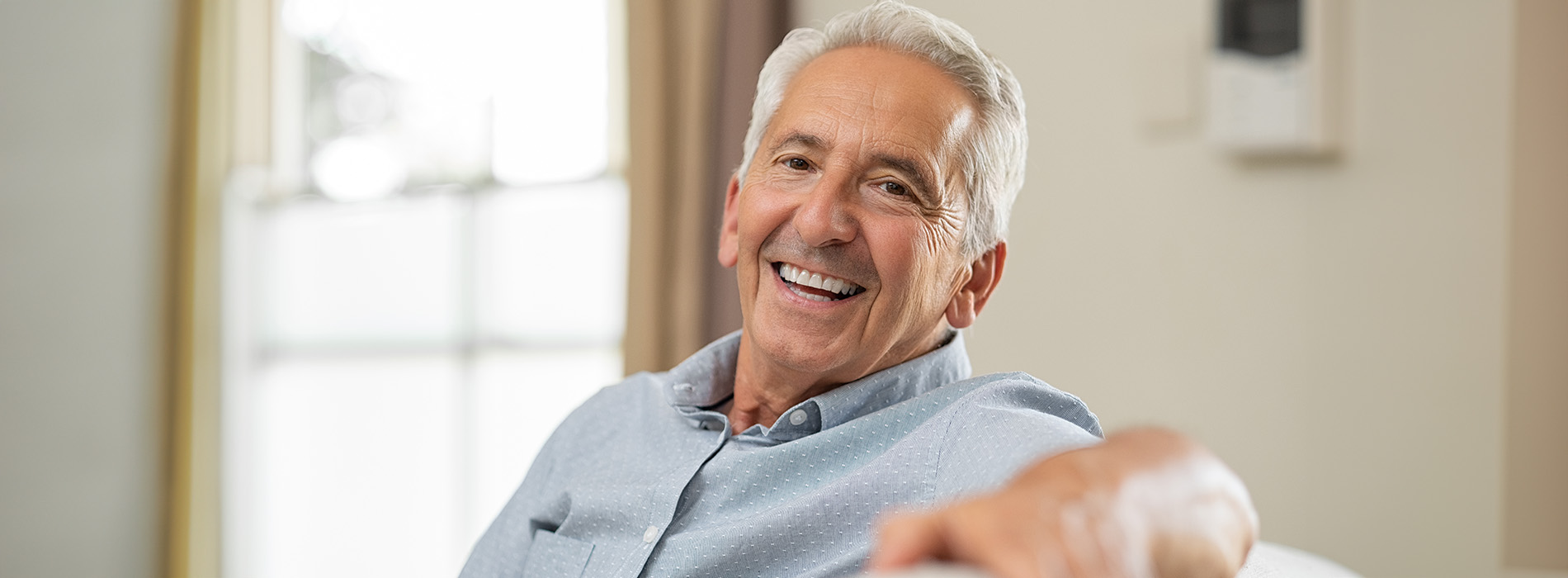 An elderly man with a smile, seated in a living room.