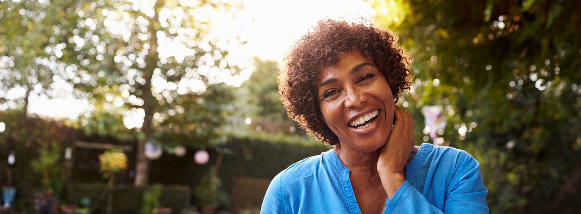 The image features a smiling woman with curly hair, wearing a blue shirt and standing outdoors.