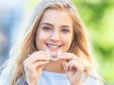 Smiling woman holding a toothbrush with braces, smiling at the camera.