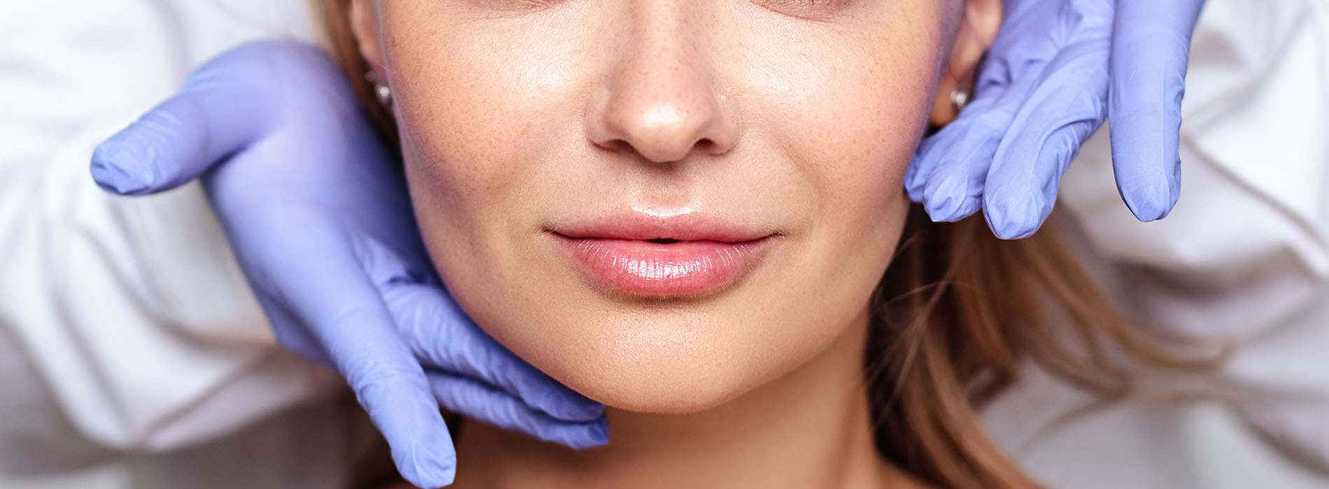 A woman receiving a facial treatment with visible blue gloves worn by the practitioner.